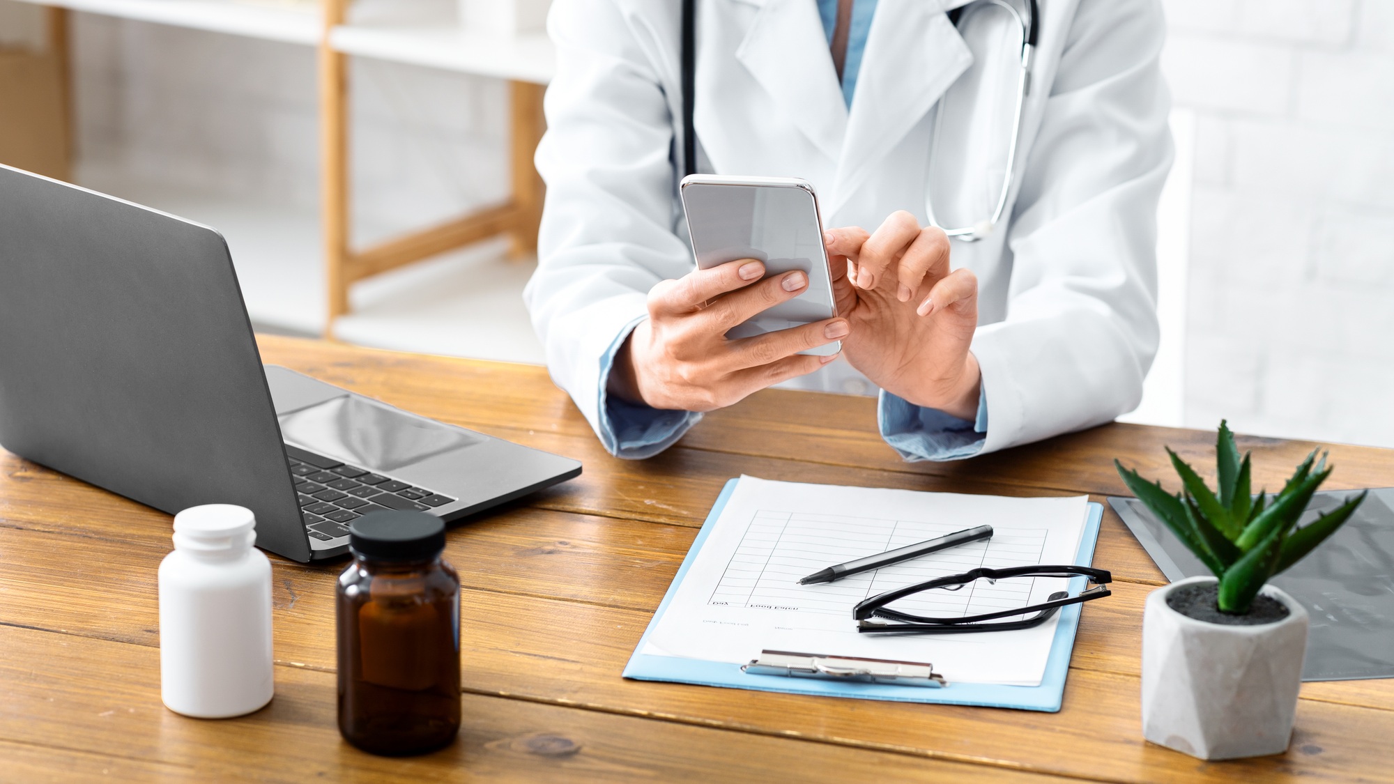 Remote online patient consultation. Female doctor typing on phone, on table